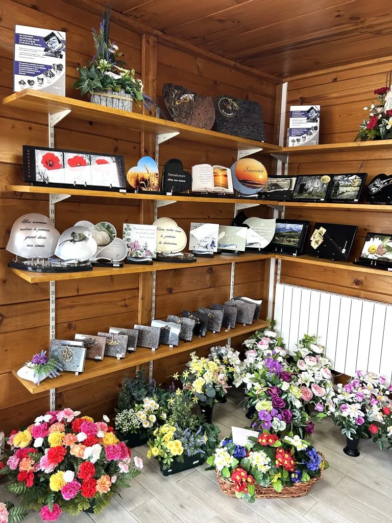 Présentation de plaques funéraires gravées et compositions florales sur des étagères en bois