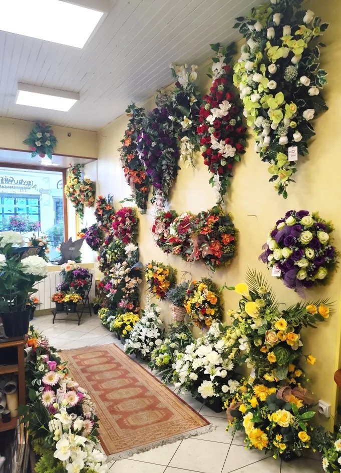 Mur d'exposition de couronnes et raquettes de fleurs artificielles dans une boutique funéraire